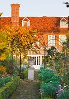 Brick path leading to house and conservatory with urn on plinth and vine in autumn colour - evening light. Saling Hall, Essex