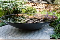 Pool with bubbles and in background stone wall with bicycle wheel rims. White viburnum to left. Tour de Yorkshire, RHS Chelsea Flower Show 2014 