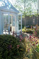 Khora architectural dome. View of the entrance to garden room with two chairs and wooden fence surrounding by Aquilegia 'Ruby port', Anemanthele lessoniana, Stipa arundinacea and Buxus. 