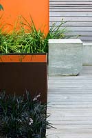 Modern contemporary garden in Brighton with square metal water feature, concrete seats on decking with wooden panel walls and orange panel 