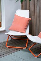 Modern contemporary garden in Brighton with white deckchairs on decking with orange cushions 