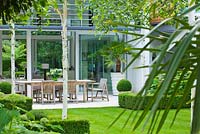 View across lawn to limestone patio with table and chairs, Betula jacquemontii - The Glass House - Architects Terry Farrell Partners - Garden design by Sallis Chandler 