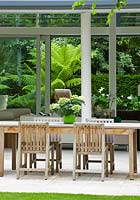 Limestone patio, table and chairs, view through glass pavilion to tree fern garden - The Glass House - Architects Terry Farrell Partners - Garden design by Sallis Chandler