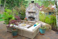 Outdoor lounge with sectional sofa, coffee table and fireplace. Teal ceramic pots planted with Acer palmatum - Japanese Maple and annual flowers.