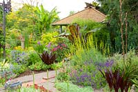 Summer mixed border with tiki house and garden art. Ensete ventricosum 'Maurelli' - Abysinnian Red Banana, Eucomis comosa 'Oakhurst' - Pineapple Lily.