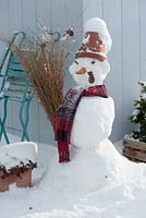 Snowman with clay pot as a hat, scarf, cabbage stalk as pipe, carrot for a nose and rose hips as eyes and mouth, broom