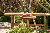 Rustic wooden bench and table with food and wine with split log wall beyond, 'Shears and Chardonnay' RHS Malvern spring festival 2014 