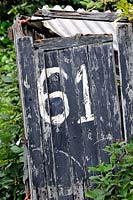 Number 61 painted on black door of crocked, distressed or run down allotment hut or shed, Golf Course Allotments, London Borough of Haringey.
