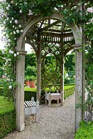 Straight gravel path overarched by tall wooden rose arbour with pink Rosa 'Awakening' - Seend, Wiltshire