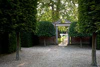 View from French-style grand pleached allee to formal gate in walled garden with stone pediment and twin topiary trees either side. Seend, Wiltshire