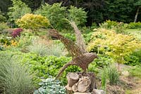 Woven willow bird with lush planting behind including hostas, silvery miscanthus and Geranium Rozanne syn. 'Gerwat', and Acer palmatum 'Sango-kaku'. Forest Lodge, Pen Selwood, Somerset, UK