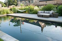 Pool garden with swimming pond, deck, hammocks and seating surrounded by naturalistic planting. Old Rectory, Batcombe, Somerset, UK