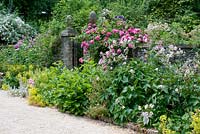 Entrance to the Victorian walled garden via acorn gates with herbaceous borders and Rosa in July - Cerney House Gardens, Cirencester