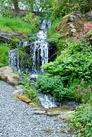 Waterfall cascading down in wild area of garden by gravel path