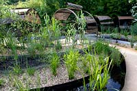 Title: Le Jardin Dechene. Pergolas made of a construction of metal hoops. Borders in plateaus planted with  Arundo donax and in the oval shaped pools aquatic plants like Menyanthes trifoliata