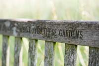 The words Loved These Gardens carved into a memorial wooden garden bench