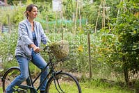 Woman leaving allotment with her bicycle and a harvest of beans