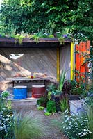 A Space To Connect and Grow. Wooden shelter area with living green roof, recycled oil drum stools, timber table, bamboo water feature, planting in water trough and recycled timber seat.