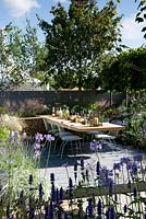 Vestra Wealth's Vista Garden. Laid dining table for outdoor entertaining set on a grey-painted decking surrounded by blue palette planting of nepeta and lavender with hydrangea Annabelle. Cool planting for hot weather. Pleached hedging. Designer: Paul Martin Sponsor: Vestra Wealth Gold award  