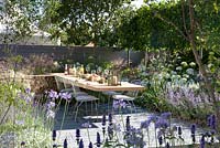 Marcus Harpur Vestra Wealth's Vista Garden. Laid dining table for outdoor entertaining set on a grey-painted decking surrounded by blue palette planting of nepeta and lavender with hydrangea Annabelle. Cool planting for hot weather. Pleached hedging. Designer: Paul Martin Sponsor: Vestra Wealth Gold award  