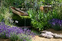 Vestra Wealth's Vista Garden Aggregate flooring with lavender planted in naturalistic style under high canopy shrubs. A small square black pool receives water from wooden channel above.  Designer: Paul Martin Sponsor: Vestra Wealth Gold award  