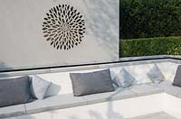 Hedge and stone wall with laser cut flower pattern by seating area 