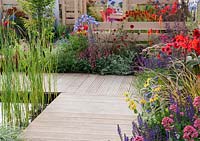 The Narrows - view of decking surrounding pond with bullrushes, mixed borders and oak fence 