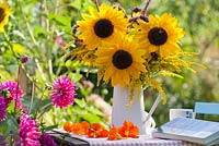 Bouquet of sunflowers and perennials Persicaria, Verbena bonariensis and Solidago in enamel jug in summer garden.