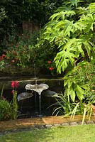 Water feature with pots and large plant of Tetrapanax. Hall Farm Garden at Harpswell near Gainsborough in Lincolnshire. August 2014.