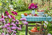 Country garden in summer with harvested vegetables and jug of perennials.