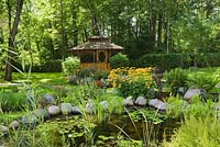 Pond with Nymphaea alba - white water lilies, Rudbeckia fulgida 'Goldsturm' - yellow coneflowers and a gazebo in the background in a backyard garden in summer, St-Colomban, Laurentians, Quebec, Canada