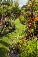 The Island - a raised bed with an exotic theme. Plants include Ricinus, Cannas, Musa basjoo and Ensete ventricosum 'Maurelii'. On the left is the Summerhouse Border. Lincolnshire. August 2014. Summer.