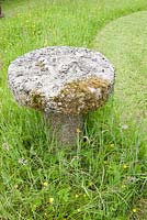 A staddle stone on a lawn that mixes cut and uncut grass in order to encourage wild flowers.