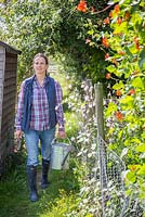 Woman entering allotment carrying watering can and hand trowel