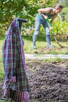 Woman digging and forking soil in an allotment patch. Focus on shirt hung on edging knife