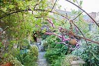 A dead tree, painted bright pink and draped with pieces of rusty metal, frames a sheltered courtyard with seating. 