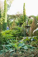A fountain surrounded by strongly shaped foliage plants including hostas, Solomon's Seal, clipped lonicera and cardoons in a courtyard garden.