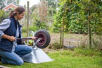 Woman inflating flat tyre on a wheelbarrow, within an allotment plot