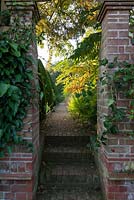 Steps leading to Rose Garden. Honeysuckle and ivy soften the brick pillars.