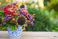 Floral display of rose hips, helianthus seed heads, verbena and chrysanthemum in blue and white tea cup