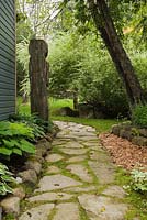 Jack-rabbit Johanssen wooden totem pole and flagstone path next to a border with Hostas in backyard garden in summer