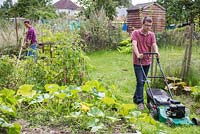 Man mowing the lawn in an allotment, woman working in the background