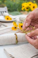 Woman making table place setting decorations using rudbeckia and stipa gigantea grass