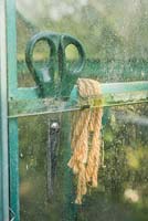 Garden scissors and twine wedged behind a greenhouse panel