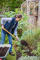 Woman mulching garden border with fresh manure