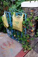NGS yellow plastic carrier bag hanging from blue gate on open day with Tropaeolum majus - Nasturtium growing through, Maynard Road, Walthamstow, London Borough of Waltham Forest