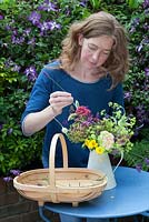 Lady making up floral display in garden using various cut blooms