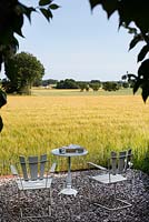 Seating area at the end of the garden looking out to a wheat field, white wooden table and chairs
