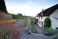 Blue sky over late summer garden planted over terraces with gravel paths and a stone cottage