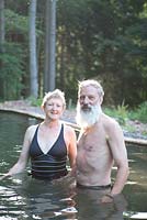 Couple standing in their natural swimming pond and the forest beyond - Sue and Ian Mabberley 